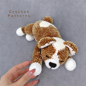 Può includere: Un giocattolo di peluche per cani in crochet di colore marrone e bianco. Il cane è sdraiato su un fianco con la testa appoggiata sulle zampe. Il cane ha una macchia bianca sul petto e orecchie bianche.