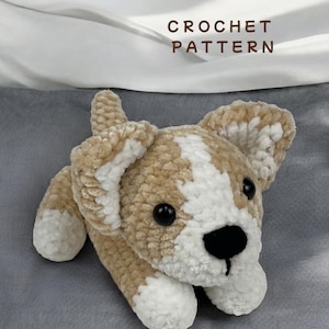 Puede incluir: Un juguete de perro tejido a ganchillo en tonos beige, blanco y negro. El perro tiene la cara y las patas blancas, las orejas y el cuerpo beige, y los ojos y la nariz negros. El texto "CROCHET PATTERN" se muestra encima del juguete.
