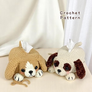 May include: Two crocheted dog-shaped tissue box covers. One is brown and white, the other is white with brown accents. Both have black eyes and brown noses.
