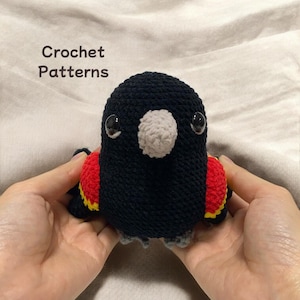 May include: A crocheted black bird with red and yellow accents. The bird has a grey beak and black eyes.
