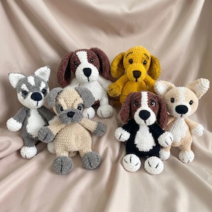 May include: A collection of six plush crochet dog toys in various colors and patterns, including a grey and white husky-style dog, a brown and white spotted dog, a solid mustard yellow dog, a beige pug, a black and white beagle, and a tan dog.