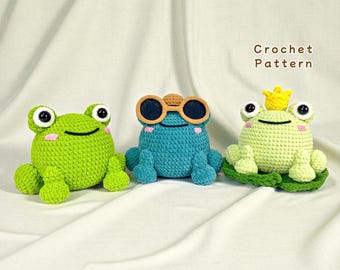 May include: Three crocheted frog toys in shades of green and blue. One frog wears sunglasses, and another wears a crown. The text "Crochet Pattern" is visible in the background. These handmade toys are perfect for children.