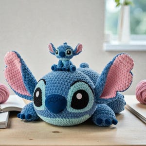 Könnte beinhalten: Ein handgefertigtes blaues Häkeltier eines Zeichentrickcharakters mit großen Ohren und einer kleinen Version desselben Charakters oben drauf. Die Ohren sind innen rosa. Das Spielzeug hat große schwarze Augen und eine blaue Nase.