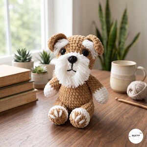 Op de afbeelding: Een gehaakt knuffeldier in de vorm van een Schnauzer-hond, met bruin garen voor het lichaam, wit garen voor de pootjes, wenkbrauwen en baard, en zwarte plastic ogen en neus. Het speelgoed heeft een getextureerd uiterlijk met zichtbare steken.