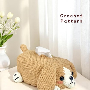 Puede incluir: Una funda de caja de pañuelos de ganchillo con forma de perro. La funda es de color marrón claro con detalles blancos y negros, que representan la cara y las patas de un perro. El texto "Crochet Pattern" es visible.