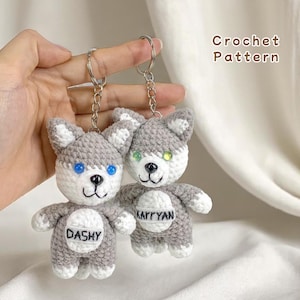 Pode incluir: Dois chaveiros de cão husky feitos à mão em crochê. Os chaveiros são cinza e branco com olhos azuis e verdes. Cada chaveiro tem um nome na barriga. O texto "Crochet Pattern" está no canto superior direito.