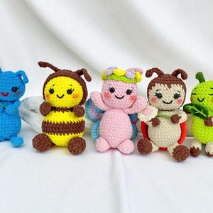 May include: Five handmade crochet insect dolls. The dolls include a blue bug, a yellow and brown bee, a pink fairy, a brown ladybug, and a green caterpillar. Each doll has a smiling face and is made of yarn.