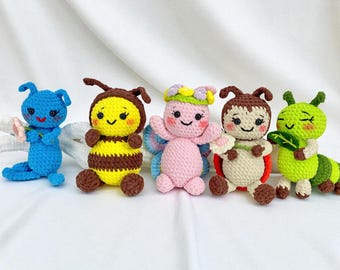 May include: Five handmade crochet insect dolls. The dolls include a blue bug, a yellow and brown bee, a pink fairy, a brown ladybug, and a green caterpillar. Each doll has a smiling face and is made of yarn.