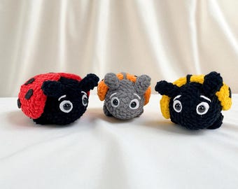 May include: Three crocheted insect toys. A red and black ladybug with black spots, a gray insect with orange accents, and a black and yellow bumblebee. Each has large white eyes and small antennae.