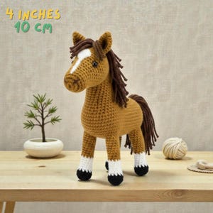 May include: A crocheted horse figurine, approximately 4 inches (10 cm) tall, in shades of brown, with a white blaze on its face and white accents on its legs. The horse has a dark brown mane and tail, and black hooves. The text "4 INCHES 10 CM" is in the top left corner.