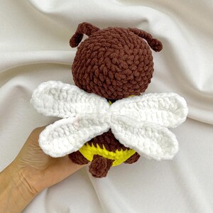 May include: A handmade crochet bee toy. The bee has a brown body, white wings, and a yellow and brown abdomen. The toy is made of soft yarn and is designed to be a cute and cuddly item.