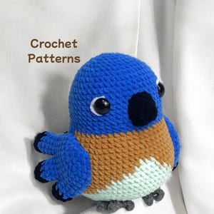 Puede incluir: Un juguete de peluche de p&aacute;jaro azul tejido a crochet con detalles marrones, blancos y azul claro. El p&aacute;jaro tiene ojos negros y un pico negro.