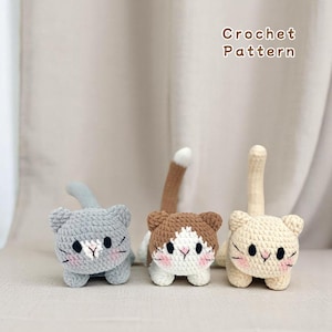 Könnte beinhalten: Drei gehäkelte Katzenspielzeuge in Grau, Braun und Creme. Jede Katze hat ein weißes Gesicht mit schwarzen Augen und einer rosa Nase. Die Katzen sitzen auf einer weißen Oberfläche. Häkelmuster.