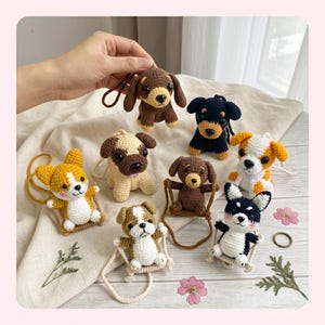 May include: A collection of seven small, crocheted dog keychains in various breeds and colors, including a brown dachshund, a black and tan dog, a yellow and white corgi, a tan pug, a brown dog on a swing, a white and brown dog, and a black and white dog.