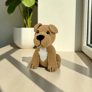 Puede incluir: Un cachorro marrón tejido a ganchillo con pecho blanco, ojos negros y nariz negra. El animal de peluche hecho a mano está sentado sobre una superficie de color claro. El perro tiene orejas pequeñas y caídas y garras cosidas en negro.