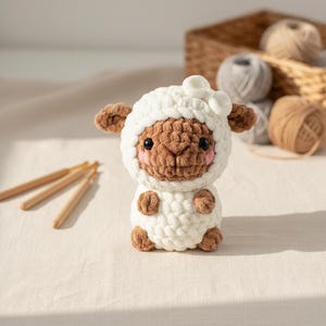 Puede incluir: Una muñeca de oveja de ganchillo hecha a mano con cuerpo blanco y cara, orejas y pies marrones. La oveja tiene mejillas rosadas y ojos negros. Ganchos de ganchillo y ovillos de lana en el fondo. La muñeca mide unos 10 cm de alto.