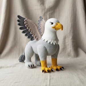 Peut inclure: Un jouet griffon crocheté à la main. La créature mythique a une tête et un cou blancs, un bec jaune et un corps gris. Les ailes sont grises, beiges et bleues. Les pattes et les pieds sont jaunes avec des griffes noires. La queue est grise.