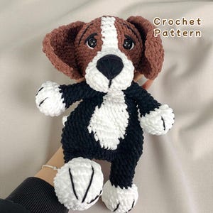 Könnte beinhalten: Ein handgefertigtes Häkeltier in Braun, Schwarz und Weiß. Der Hund hat Schlappohren, eine schwarze Nase und eine weiße Brust. Der Text "Crochet Pattern" ist im Bild zu sehen.