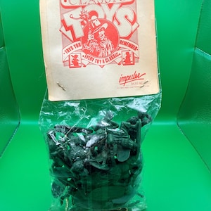 以下が含まれることがあります： 緑色のプラスチック製おもちゃの兵隊が入った密封されたパッケージ。パッケージには、カウボーイのイラストとともに「CLASSIC TOYS」と書かれています。パッケージのテキストには「TAKE-HOME-A-MEMORY」と「EVERY TOY A CLASSIC」が含まれています。3歳未満のお子様にはお勧めできません。