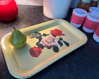 May include: A vintage yellow rectangular tray with a floral rose design. A green pear sits on the tray. Red and white gingham-wrapped candle holders and a red apple are also visible.