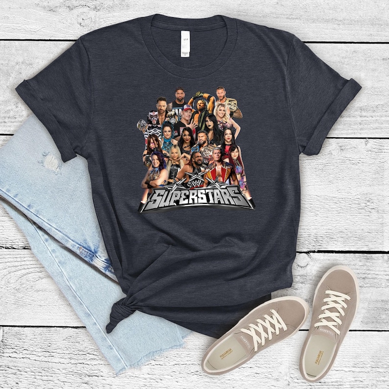 May include: Dark gray t-shirt featuring a group of WWE Superstars. The shirt displays the WWE Superstars logo in silver and white. The shirt is paired with light gray sneakers and blue jeans.