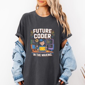 May include: Dark gray t-shirt with a colorful graphic that reads "FUTURE CODER" above an illustration of a person coding. The text "IN THE MAKING" is below the illustration. The person is sitting at a desk with computer screens.