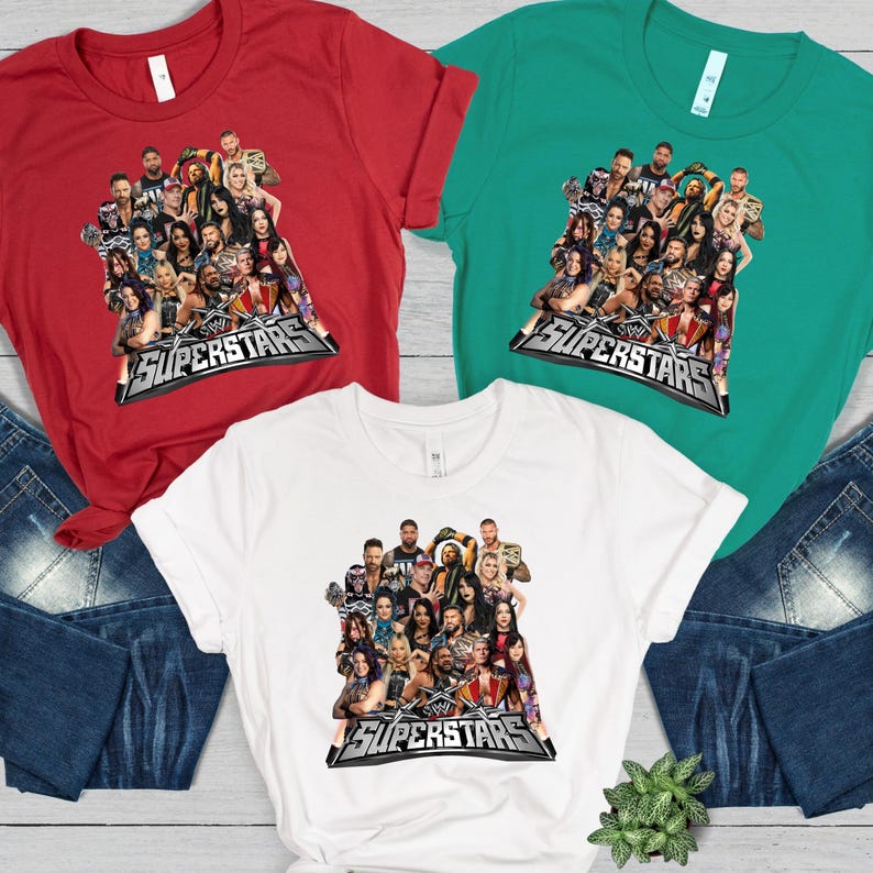 May include: Three t-shirts in red, green, and white, each featuring a graphic of multiple wrestlers. The graphic includes the text "WWE SUPERSTARS" in a silver and black design. The shirts are displayed with blue jeans.