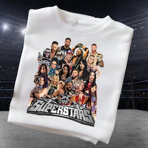 May include: White crew neck sweatshirt featuring a graphic of multiple wrestling superstars. The graphic includes the text "SUPERSTARS" in silver and black. The sweatshirt is made of a soft material.