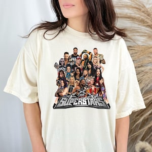 May include: Cream-colored t-shirt featuring a graphic of multiple WWE Superstars. The design includes the WWE logo and the word "SUPERSTARS" in a silver and black banner. The shirt is a casual, unisex style.