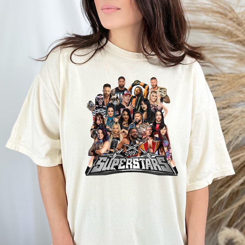 May include: Cream-colored t-shirt featuring a graphic of multiple WWE Superstars. The design includes the WWE logo and the word "SUPERSTARS" in a silver and black banner. The shirt is a casual, unisex style.
