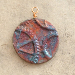 May include: A round, copper-colored pendant with a textured surface and a copper wire loop for hanging. The pendant has a blue and brown color scheme.