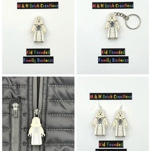 Op de afbeelding: Een verzameling handgemaakte items met een Lego-achtige figuur. De items omvatten een op zichzelf staande figuur, een sleutelhanger, een ritstrekker en een paar oorbellen. De figuur is wit met een patroonjurk. De tekst "M & H Brick Creations" en "Kid Founded Family Business" is ook zichtbaar.