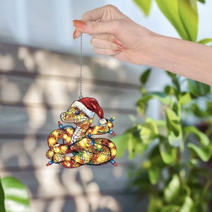 Puede incluir: Un adorno navide&ntilde;o con forma de serpiente que lleva un gorro de Pap&aacute; Noel y est&aacute; envuelto en luces navide&ntilde;as de colores.