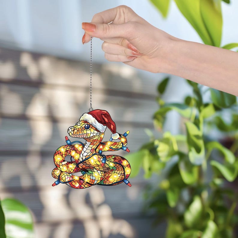 Puede incluir: Un adorno navide&ntilde;o con forma de serpiente que lleva un gorro de Pap&aacute; Noel y est&aacute; envuelto en luces navide&ntilde;as de colores.