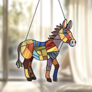Puede incluir: Un burro de vidrio coloreado con un dise&ntilde;o de patchwork en tonos de rojo, amarillo, azul, verde y morado. El burro est&aacute; colgado de una cadena negra.