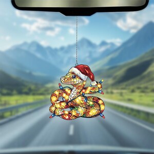 Puede incluir: Una serpiente amarilla y naranja que lleva un gorro de Pap&aacute; Noel rojo con luces de colores envueltas a su alrededor. La serpiente es un amuleto de coche que cuelga del espejo retrovisor.