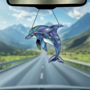 Puede incluir: Un adorno de coche de cristal de colores con forma de delf&iacute;n en azul, morado y verde. El delf&iacute;n est&aacute; saltando fuera del agua con la cola hacia arriba.