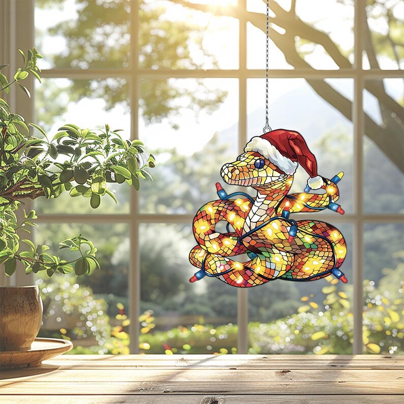 Puede incluir: Un adorno de serpiente de vidrio tintado con un gorro de Pap&aacute; Noel y luces de Navidad envueltas a su alrededor. La serpiente es amarilla, naranja y roja con un patr&oacute;n de mosaico.