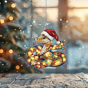 Puede incluir: Un adorno navide&ntilde;o de vidrio emplomado con una serpiente que lleva un gorro de Pap&aacute; Noel y est&aacute; envuelta en luces navide&ntilde;as.