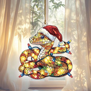 May include: A stained glass Christmas ornament of a snake wearing a Santa hat and wrapped in Christmas lights.