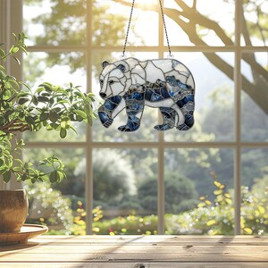 May include: A stained glass window hanging with a blue and white bear design. The bear is walking and has a mountain scene in the background.