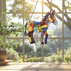 Puede incluir: Un burro de vidrio coloreado con un dise&ntilde;o de patchwork. El burro est&aacute; colgado de una cadena frente a una ventana.