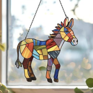 Puede incluir: Un burro de vidrio coloreado con un dise&ntilde;o de patchwork en tonos de rojo, amarillo, azul, verde y morado. El burro est&aacute; colgado de una cadena de metal negro.
