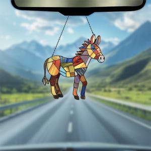 Puede incluir: Un burro de vidrio de colores que cuelga de un espejo retrovisor. El burro est&aacute; hecho de varios tonos de azul, rojo, amarillo y verde.