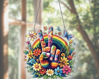 May include: A colorful peace sign decoration featuring a rainbow, flowers, and butterflies. The hand gesture is painted with vibrant colors and floral patterns. The sign is surrounded by a wreath of flowers and greenery, and is suspended by a chain.
