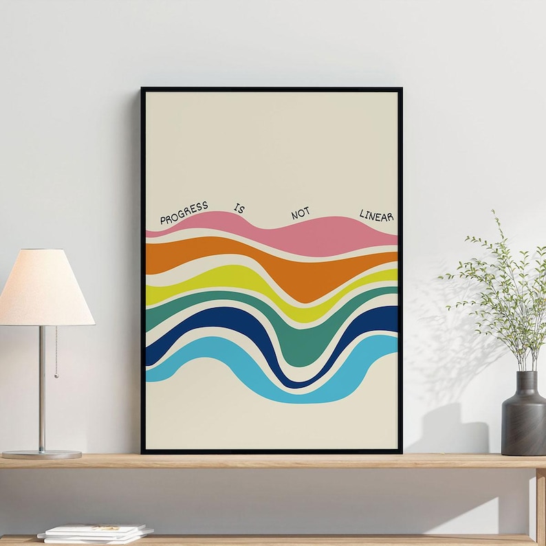 May include: A framed art print with a cream background and a colorful wavy design. The design includes waves of pink, orange, yellow, green, blue, and light blue. The words "PROGRESS IS NOT LINEAR" are printed across the top of the design in black.