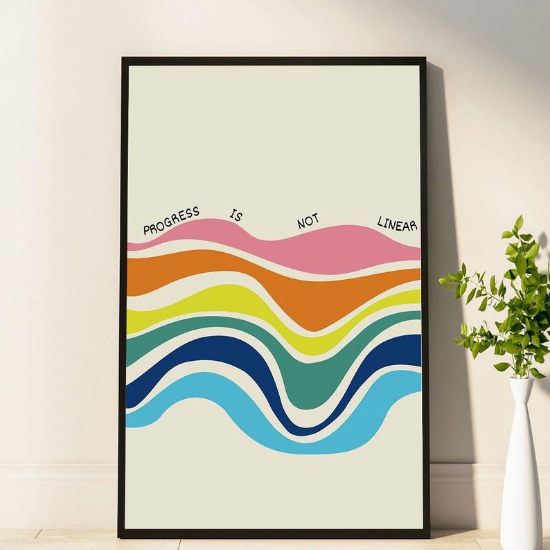 May include: A framed art print with the words "Progress is Not Linear" above colorful, wavy bands. The bands include pink, orange, yellow, green, blue, and teal. The background is a light beige color.