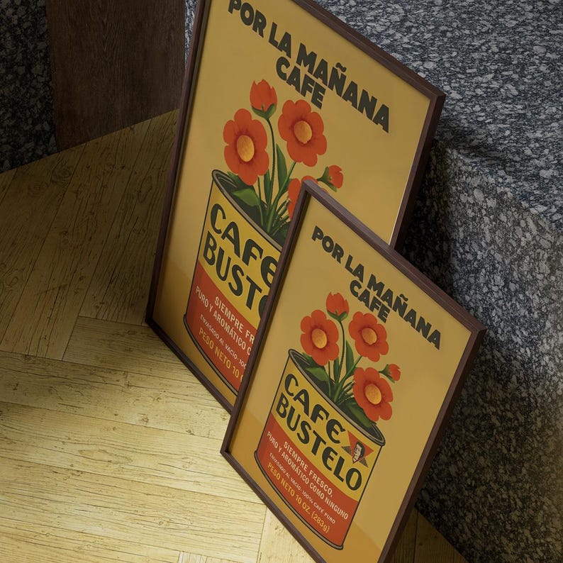 Pode incluir: Dois cartazes emoldurados com um an&uacute;ncio de caf&eacute; vintage. Os cartazes apresentam um fundo amarelo com uma ilustra&ccedil;&atilde;o de lata de caf&eacute; e flores vermelhas. O texto inclui "CAFE BUSTELO" e "POR LA MA&Ntilde;ANA CAFE".