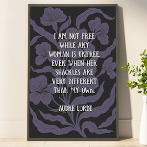 May include: A framed art print with a black background and purple floral design. The print features the quote "I AM NOT FREE WHILE ANY WOMAN IS UNFREE, EVEN WHEN HER SHACKLES ARE VERY DIFFERENT THAN MY OWN. AUDRE LORDE" in white text.