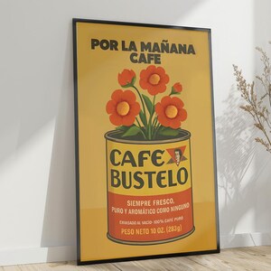 Pode incluir: Um poster emoldurado com fundo amarelo apresenta um design de lata de caf&eacute; com o texto "CAFE BUSTELO". A lata cont&eacute;m flores laranja. O texto superior diz "POR LA MA&Ntilde;ANA CAFE". O texto inferior diz "PESO NETO 283g (10 oz)."